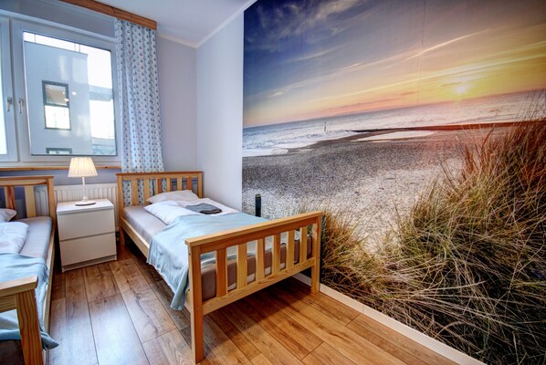 A bedroom with a wooden bed, a nightstand, a lamp, and a window with curtains. - HelApartamenty - Apartament Baltyk II (Hel)