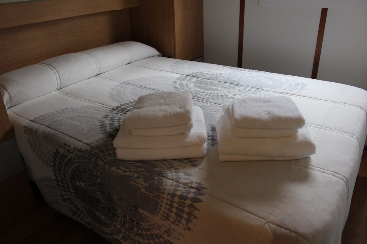 A neatly made bed with a patterned bedspread and two stacks of folded towels.