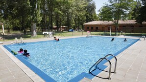 En rektangulär swimmingpool med en kakelbeklädd poolkant, omgiven av träd och en byggnad med ett kaklat tak.