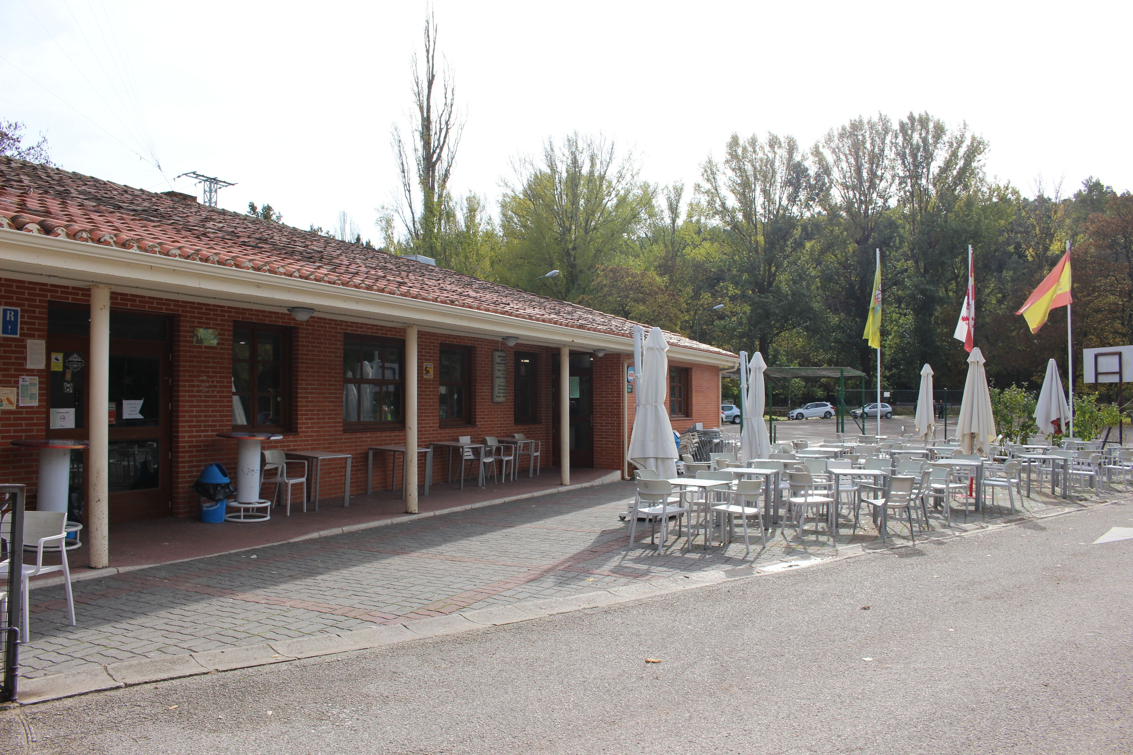 A building with a tiled roof, outdoor seating area with tables and chairs, and flags.