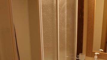 Une salle de bain avec une douche à parois de verre, un lavabo doté d’un distributeur de savon et un miroir au-dessus du lavabo.