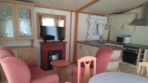 Ett kompakt bostadsutrymme med ett litet kök, en tv, ett matbord och två soffor.