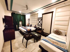 A hotel room with a bed, a desk, a chair, a TV, and a ceiling fan. - Unistar Rooms (New Delhi)