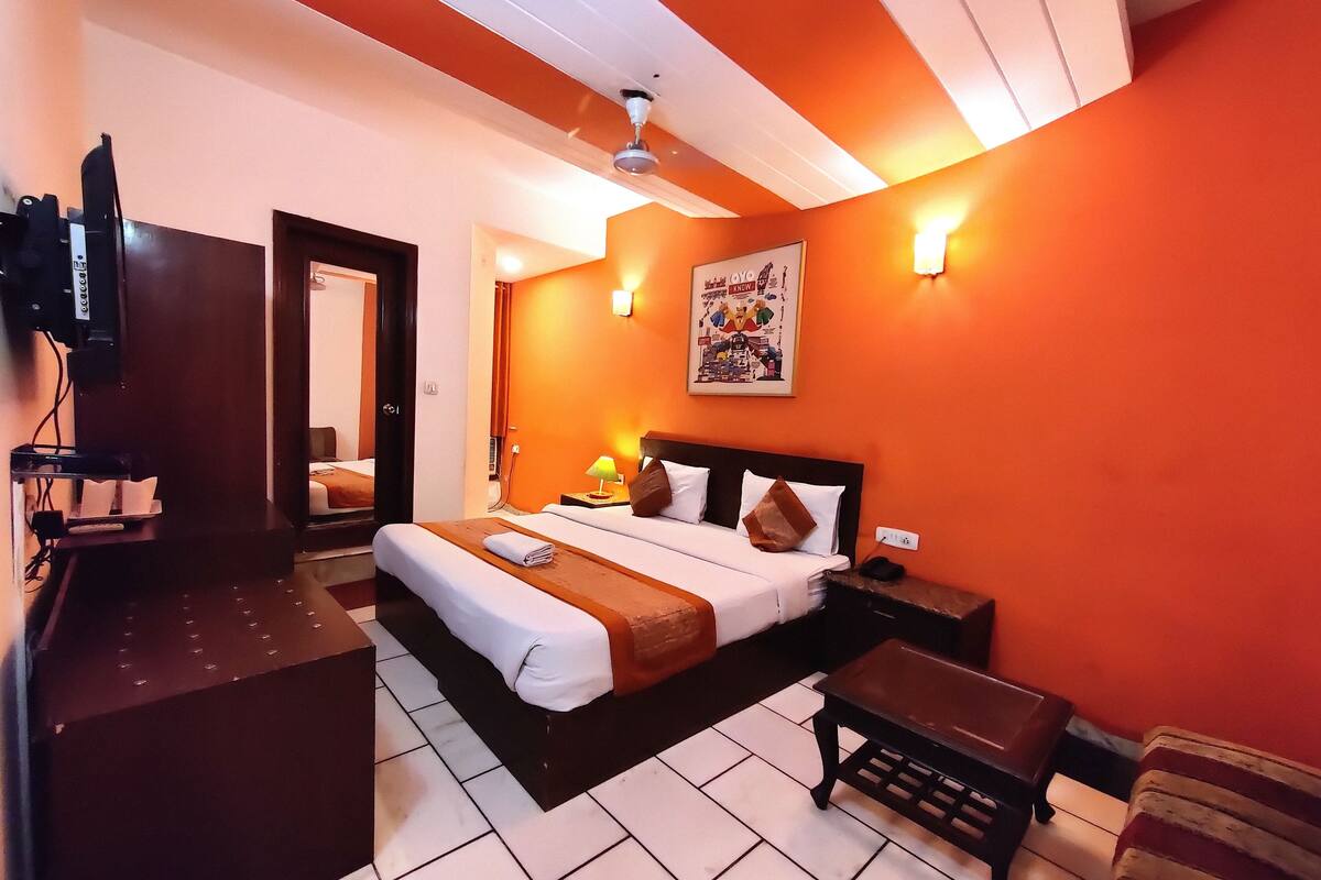 A hotel room with a bed, bedside table, lamp, and a poster on the wall.