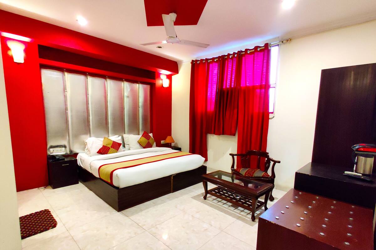 A hotel room with a bed, a chair, a desk, and a window with red curtains.