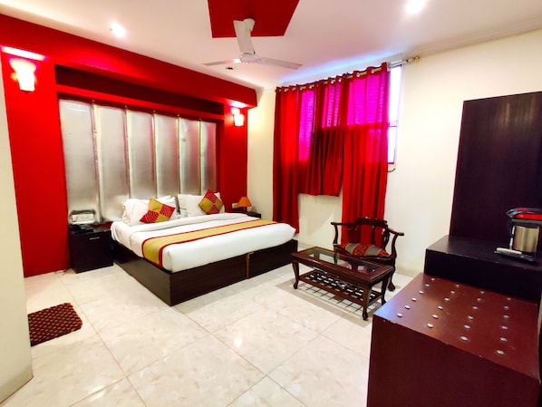 A hotel room with a bed, a chair, a desk, and a window with red curtains.