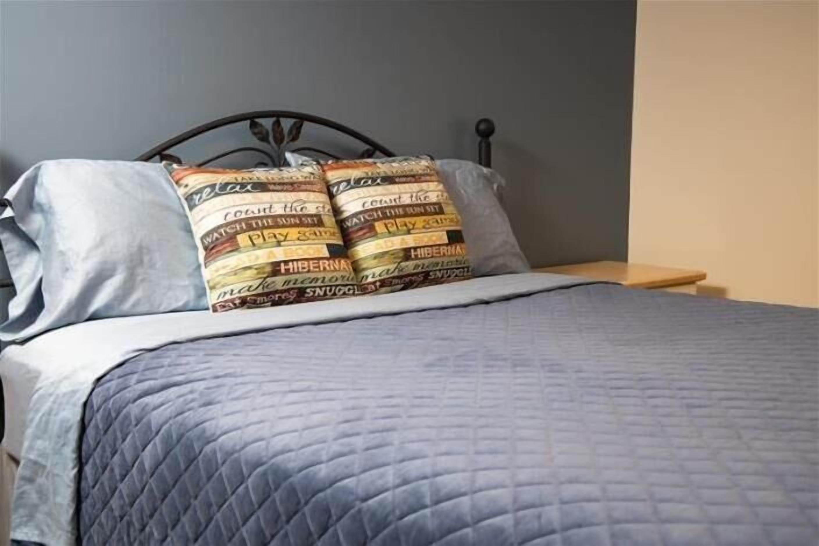 Un lit avec une couverture matelassée bleue et deux oreillers ornés de motifs textuels.
