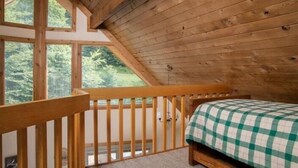 A wooden cabin bedroom with a bed, a wooden railing, and a view of the forest. - NF31-Slopeside Home! Hot Tub! A/C, Fire Pit! (Davis)