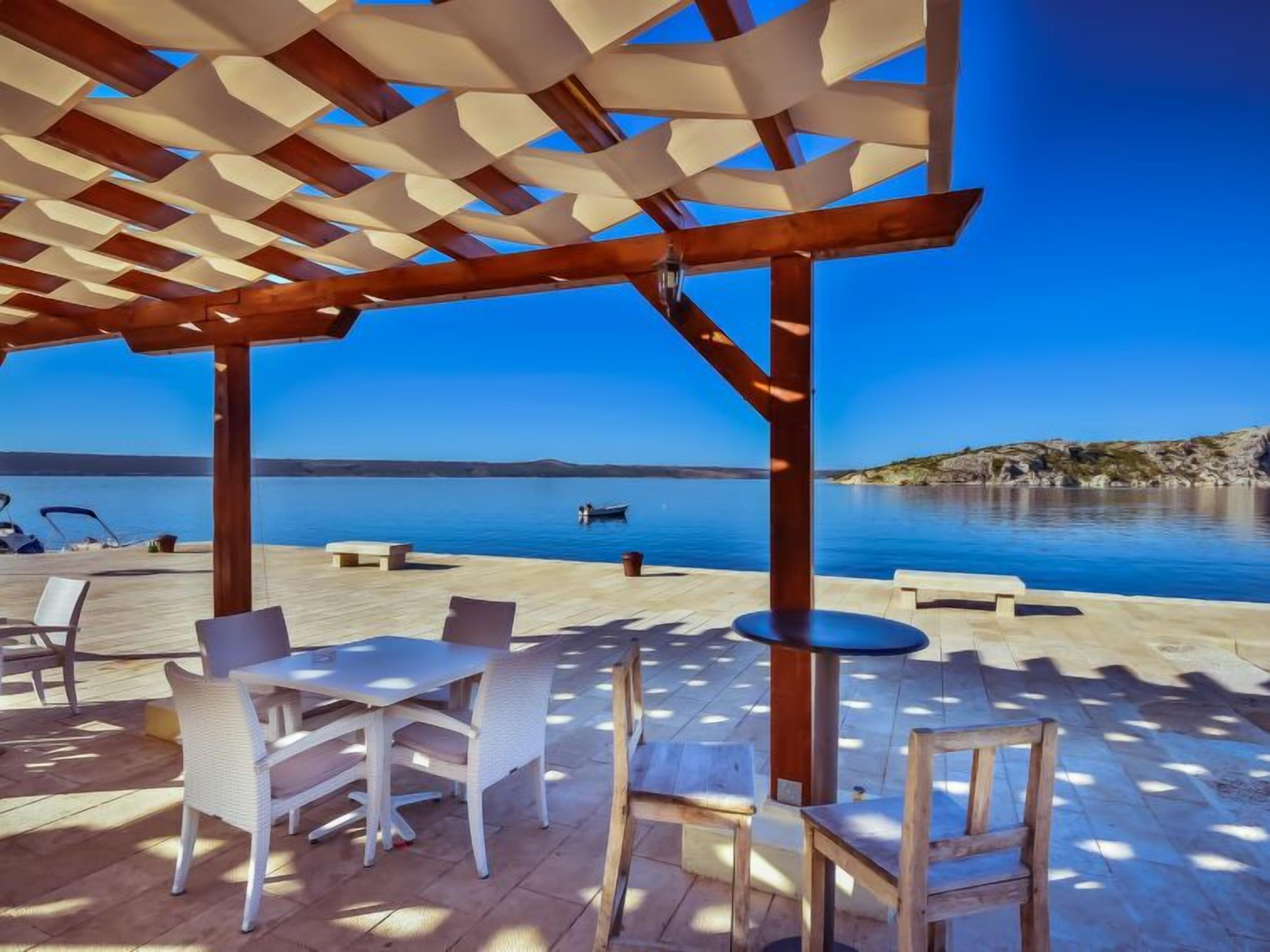 An outdoor terrace with a pergola, seating, and a view of the sea.