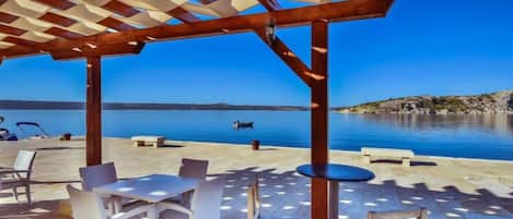 An outdoor terrace with a pergola, seating, and a view of the sea.