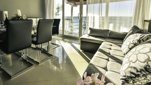 Een moderne woonkamer met een bank, stoelen, een eettafel en een groot raam met uitzicht op zee.