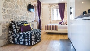 Une pièce avec un mur en pierre, un lit, un canapé et un téléviseur fixé au mur.