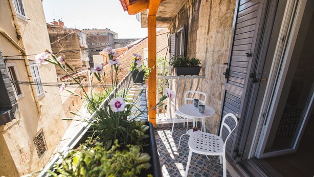 Un balcon agrémenté de plantes en pot, une chaise blanche et une petite table ronde.