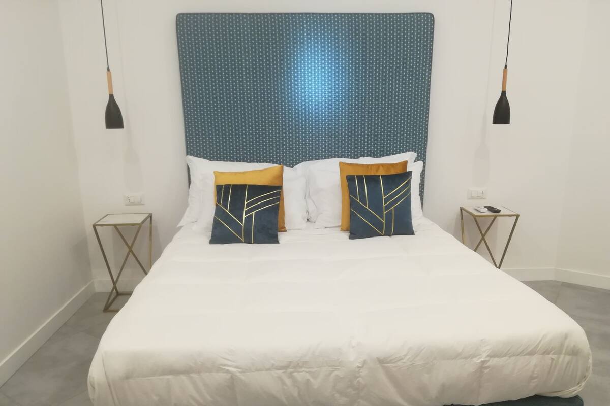 A neatly made bed with white bedding, two bedside tables, and a blue patterned headboard.