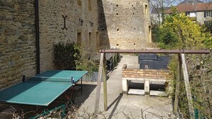 A courtyard with a stone building, a ping pong table, and a brick bench. - Large gîte with indoor swimming pool (Charbogne)