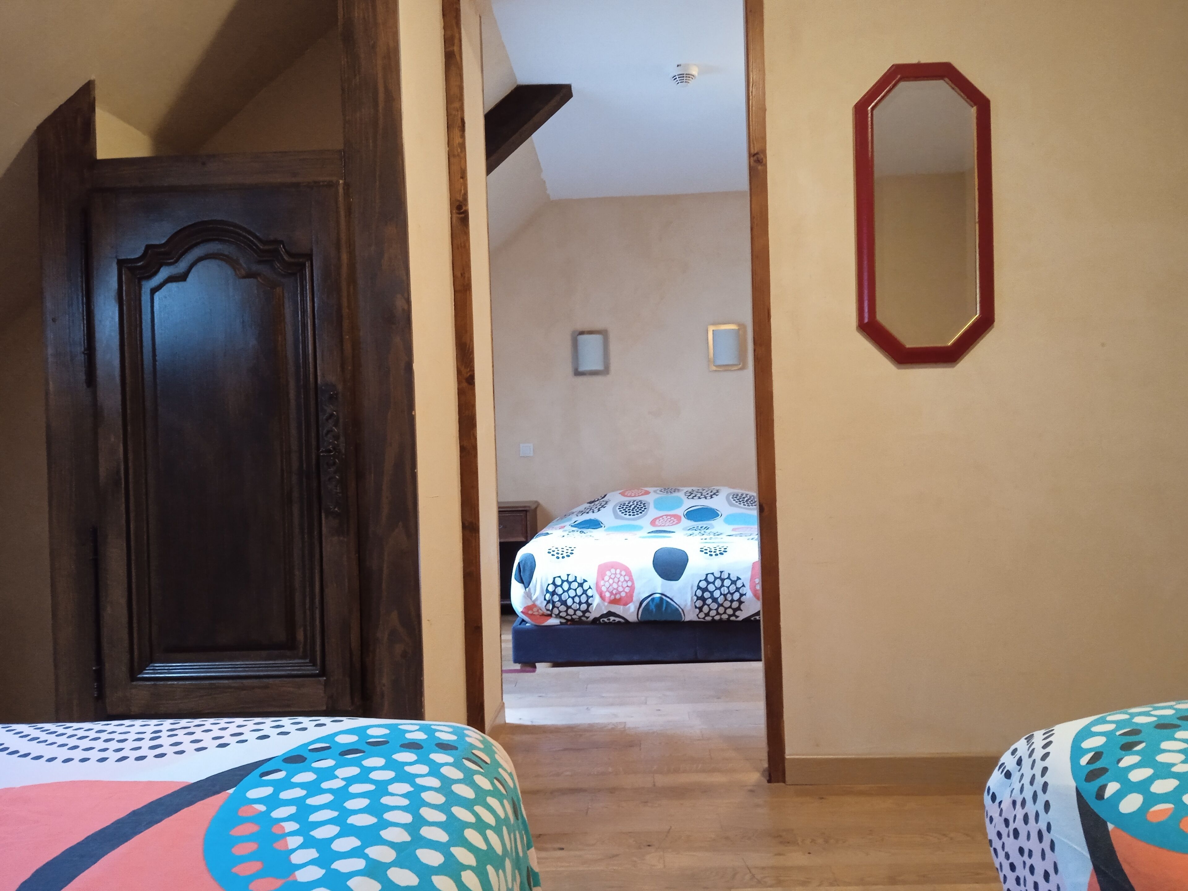 A room with a wooden door, a bed with a colorful patterned bedspread, and a mirror on the wall.