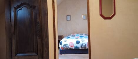 A room with a wooden door, a bed with a colorful patterned bedspread, and a mirror on the wall.