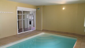 A swimming pool with a clear view of a sliding glass door leading to a room with a closet and a small window. - Large gîte with indoor swimming pool (Charbogne)