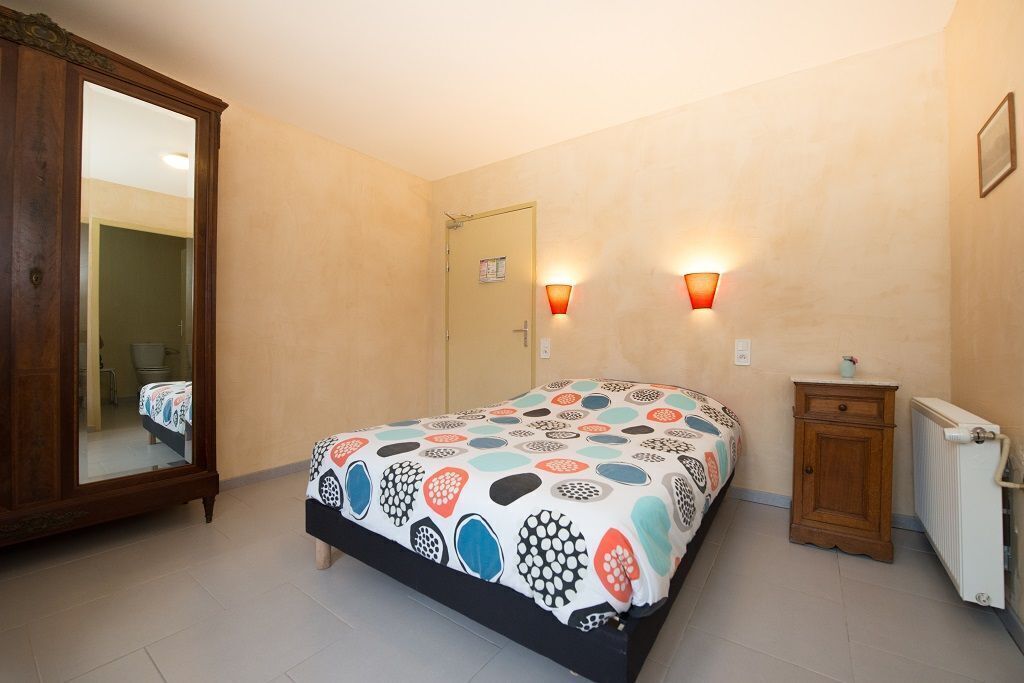 Een slaapkamer met een bed, een houten garderobe, een klein kastje, een radiator en twee wandlampen.