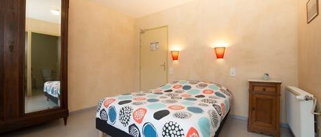 Een slaapkamer met een bed, een houten garderobe, een klein kastje, een radiator en twee wandlampen.