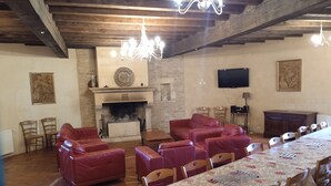A spacious room with a fireplace, leather sofas, a dining table, and wooden chairs. - Large gîte with indoor swimming pool (Charbogne)