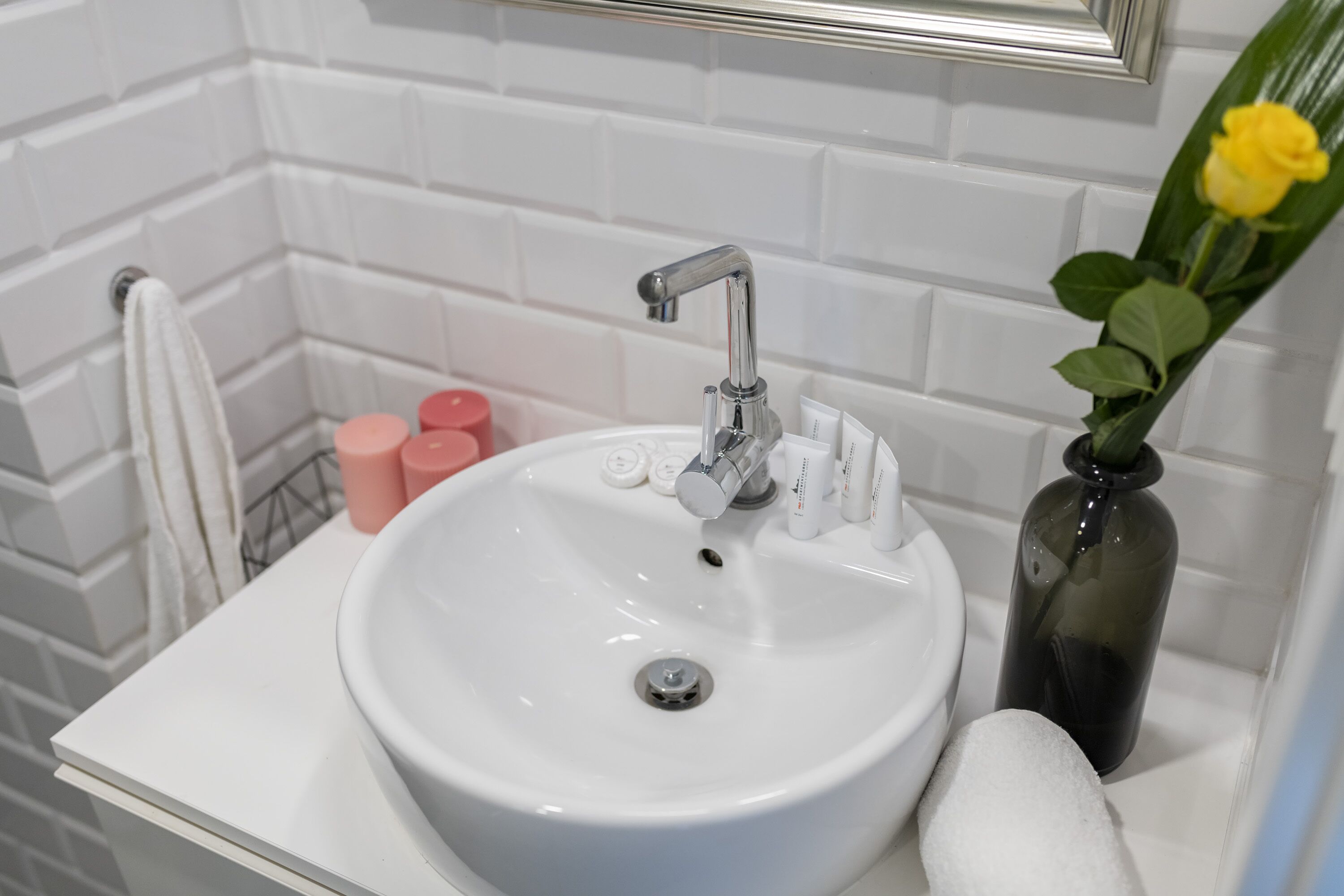 A bathroom with a white sink, a mirror above it, and a vase with a yellow flower.