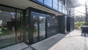 A modern building with large glass doors, a paved entrance area, and a clear view of the surrounding trees and sky. - P&O Apartments Metro Wilanowska 4 (Warsaw)