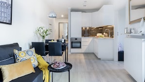 A modern living room with a sofa, a dining table, and a kitchen in the background. - P&O Apartments Metro Wilanowska 4 (Warsaw)