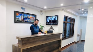 Un mostrador de recepción con detalles de madera, una obra de arte con vista a la ciudad enmarcada encima y una pantalla digital en la pared.