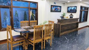 Una zona de recepción con un mostrador de madera, una mesa de vidrio con sillas y un ventanal con vistas a árboles.