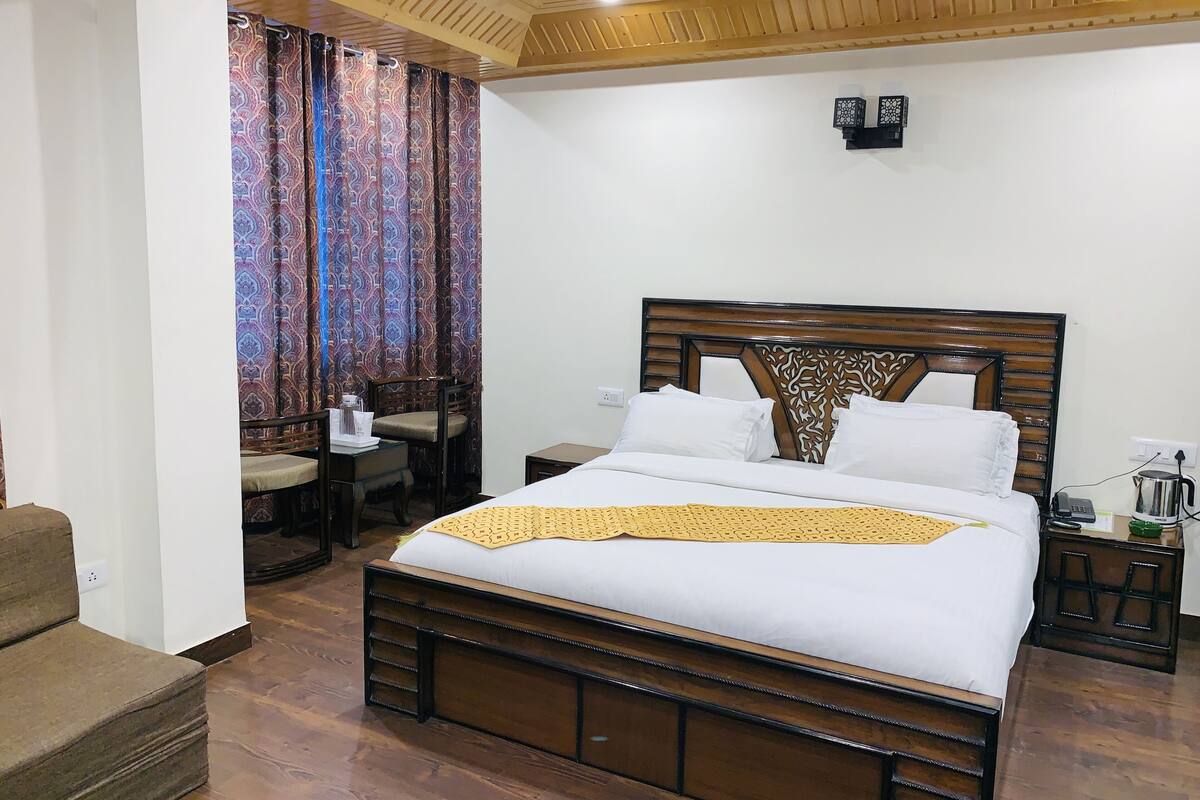 A neatly arranged hotel room with a wooden bed, a small table with a chair, and a patterned curtain.