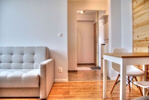 A modern living room with a grey sofa, a wooden dining table, and a white chair. - HelApartamenty - Apartament Baltyk III (Hel)