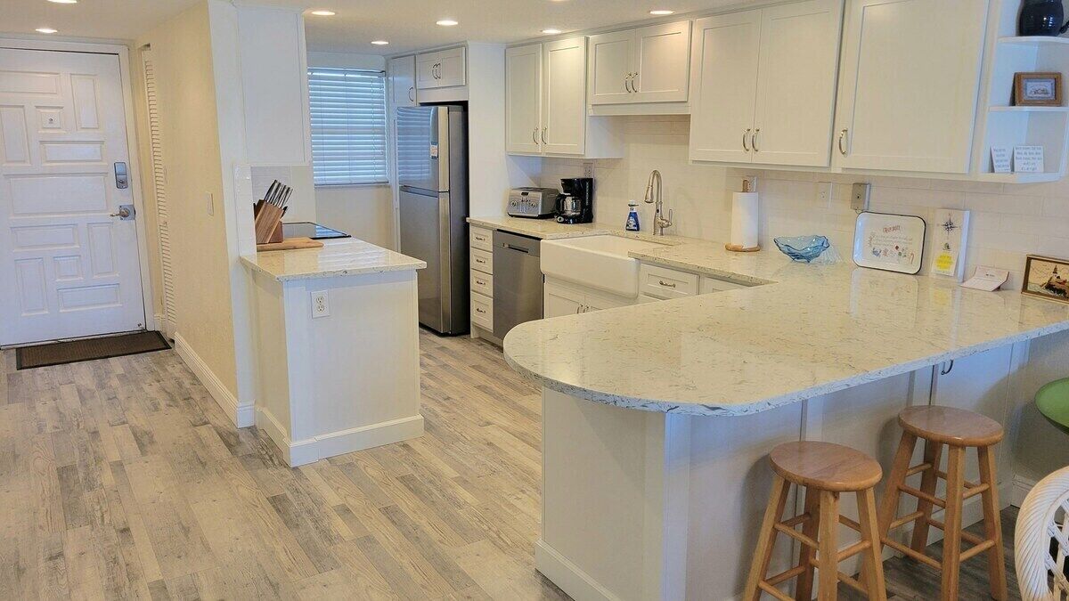 Una cocina moderna con muebles blancos, un refrigerador de acero inoxidable, un lavavajillas y una isla grande con taburetes.