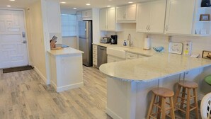 Een moderne keuken met witte kasten, een koelkast van roestvrij staal, een vaatwasser en een groot eiland met krukken.