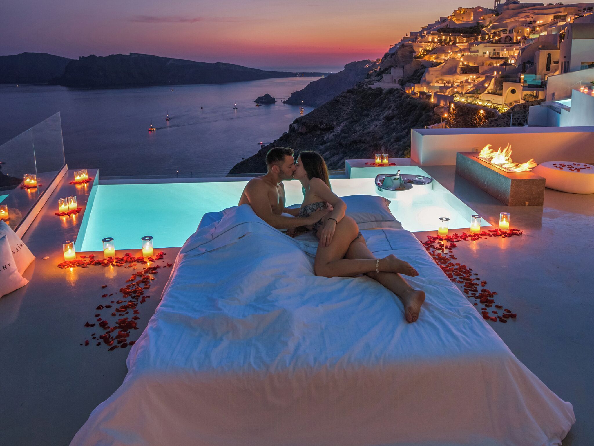 Una pareja en una cama con vistas a un pueblo costero al atardecer.