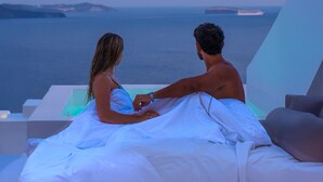 Una pareja sentada en una cama con vistas al mar y a las islas.