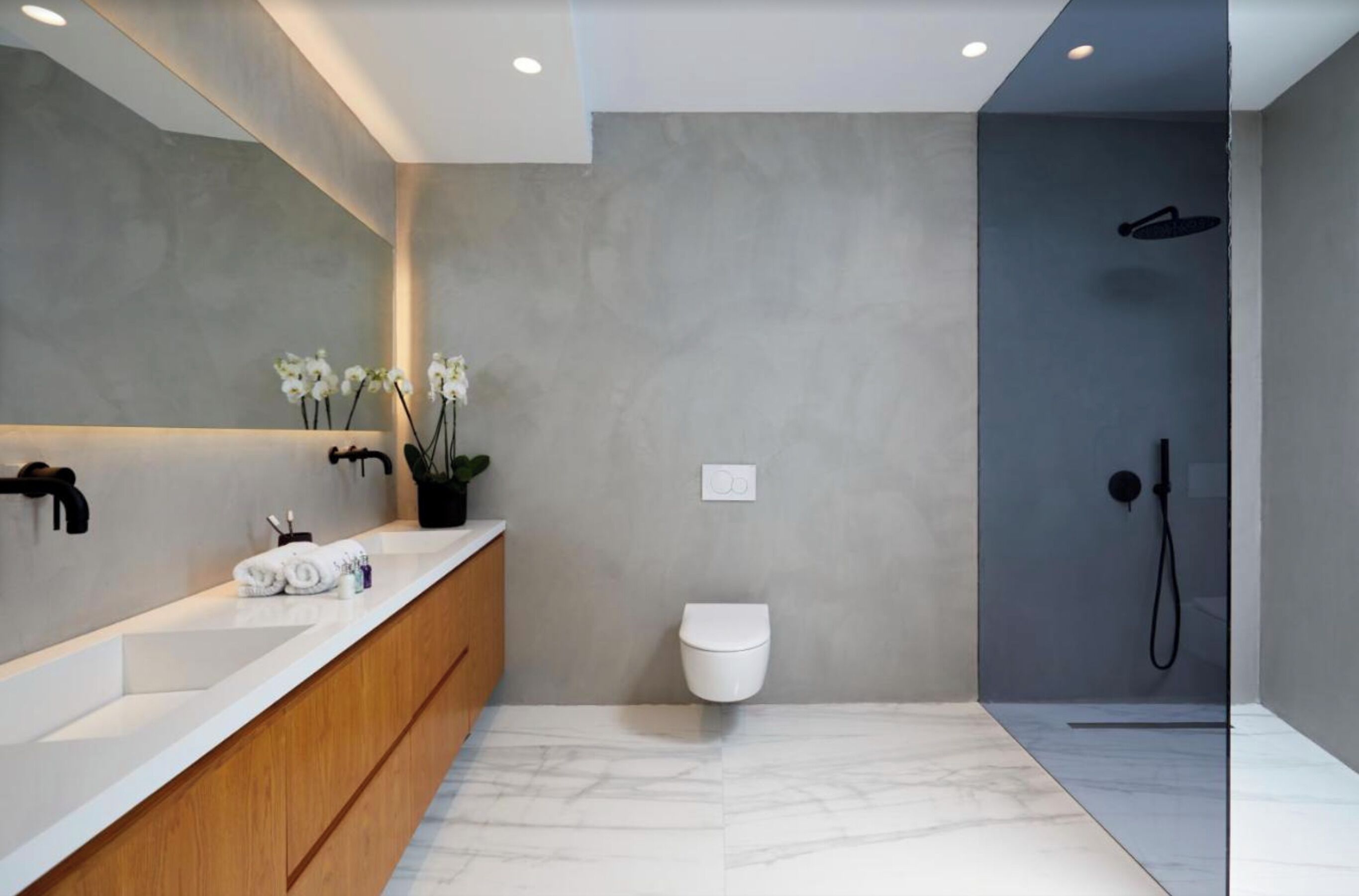 Un baño moderno con un espejo grande, un tocador de madera, un inodoro blanco y una zona de ducha con mampara de vidrio.