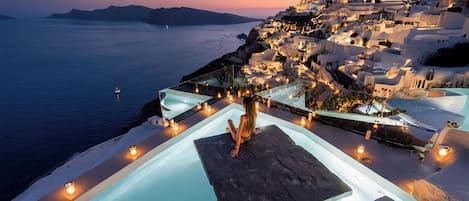 Un hotel frente al mar con piscina infinita, arquitectura blanca y vista al océano al anochecer.