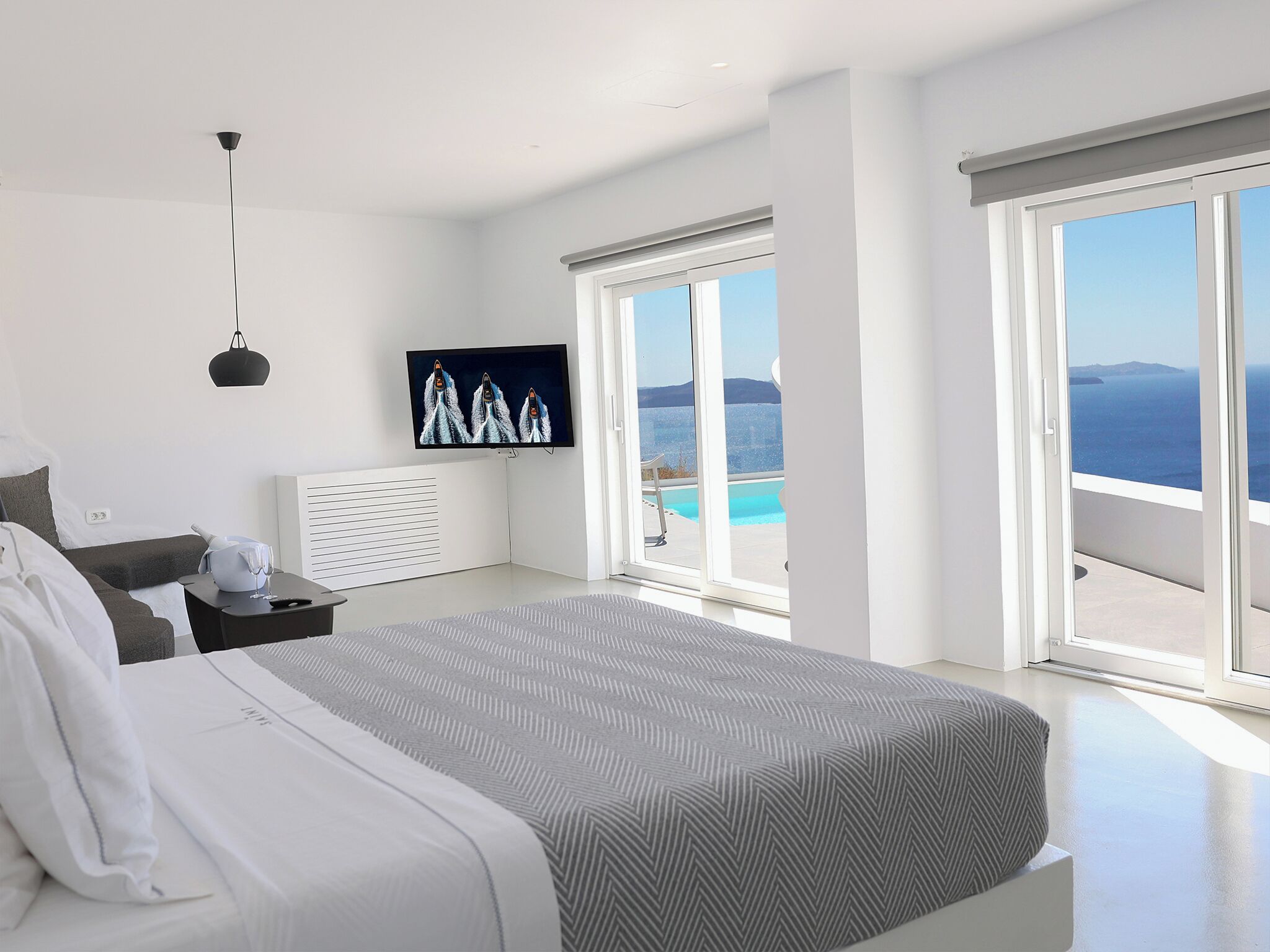A modern bedroom with a bed, a TV, a window with a view of the sea, and a balcony.