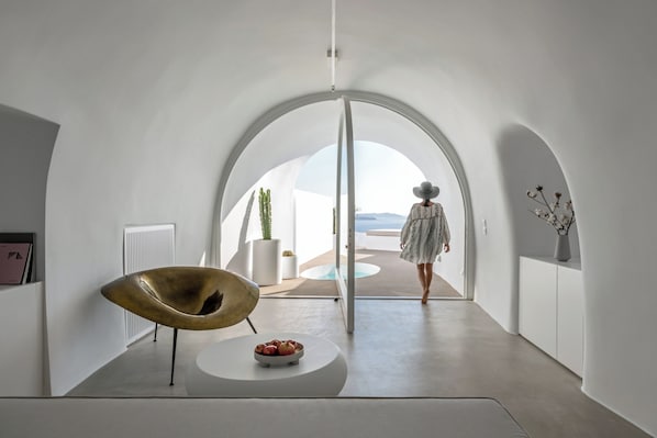 Een modern interieur met een gebogen plafond, een centraal zitgedeelte met een schaal fruit, en uitzicht op de omgeving.