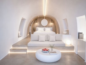 A modern bedroom with a large bed, a round light fixture, and a round coffee table with books and apples.