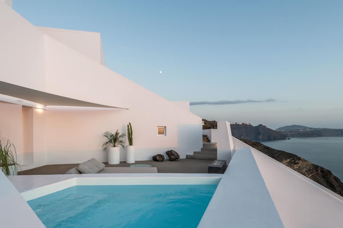 A modern outdoor pool area with a view of the sea and mountains.