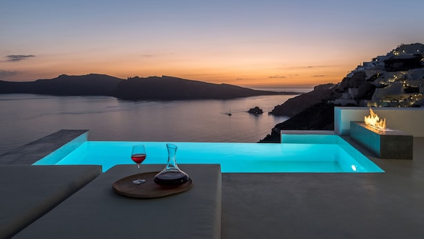 Vista del atardecer desde una zona de piscina, con una copa de vino tinto y una vela sobre la mesa.