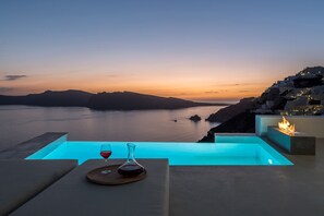 Vista del atardecer desde una zona de piscina, con una copa de vino tinto y una vela sobre la mesa.