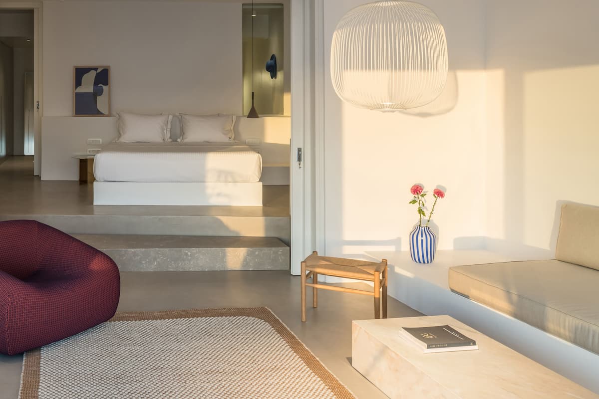 A modern bedroom with a large bed, bedside table, and a small wooden stool.