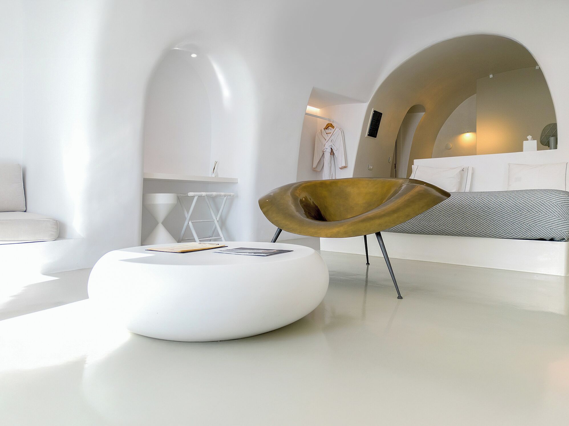 A modern living room with a white sofa, a unique gold-colored chair, and a white ottoman.