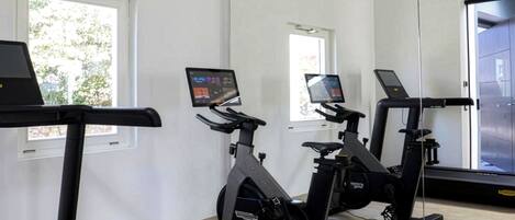 Un gimnasio con bicicletas estáticas, una cinta de correr y un espejo grande.