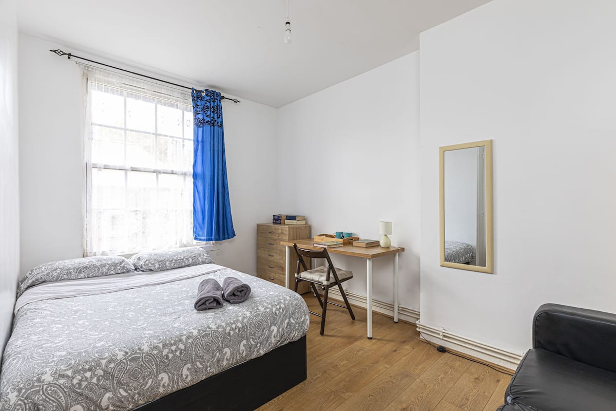 A bedroom with a bed, a desk, a chair, a mirror, and a window with curtains.