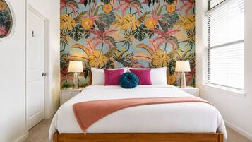 A bedroom with a bed, two bedside lamps, a wall mural, and a window with blinds.