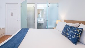 Une chambre d’hôtel avec un lit, une table de chevet, une lampe et une salle de bain visible à travers une porte en verre.